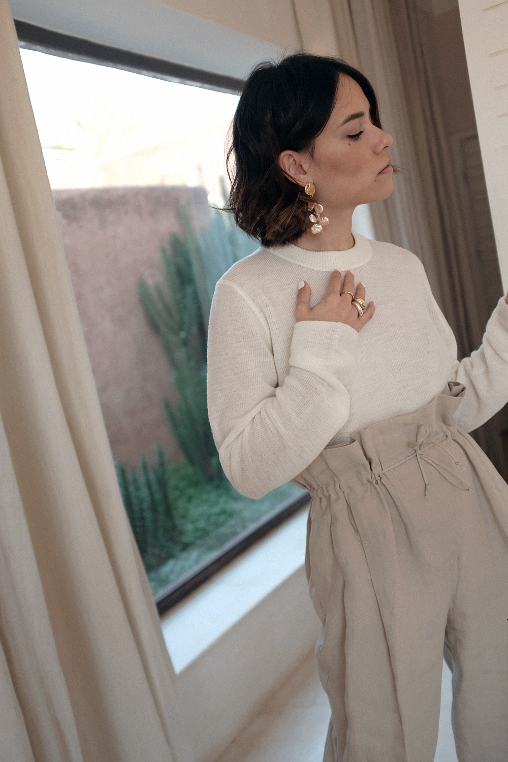 Nisi is wearing: Acne Studios Paperbag pants, Céline strap sandals, Wool crew neck shirt, The Row Ascot bag, Alighieri La Jetée earrings