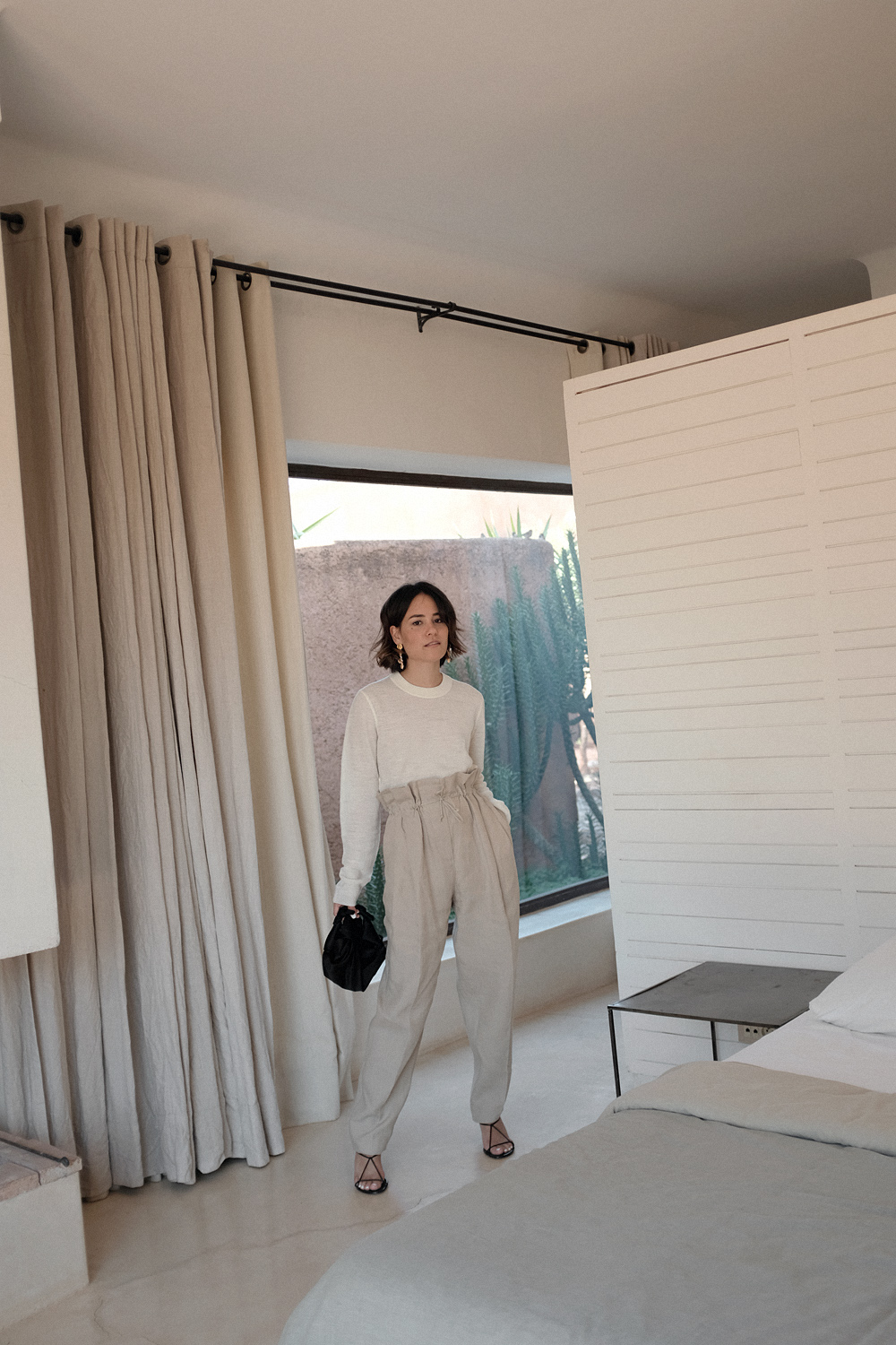 Nisi is wearing: Acne Studios Paperbag pants, Céline strap sandals, Wool crew neck shirt, The Row Ascot bag, Alighieri La Jetée earrings