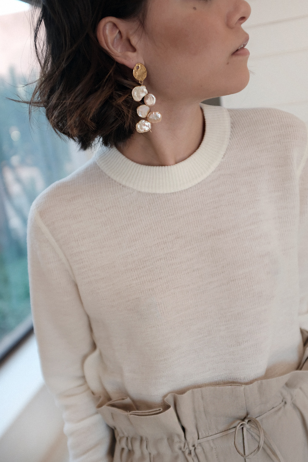 Nisi is wearing: Acne Studios Paperbag pants, Céline strap sandals, Wool crew neck shirt, The Row Ascot bag, Alighieri La Jetée earrings