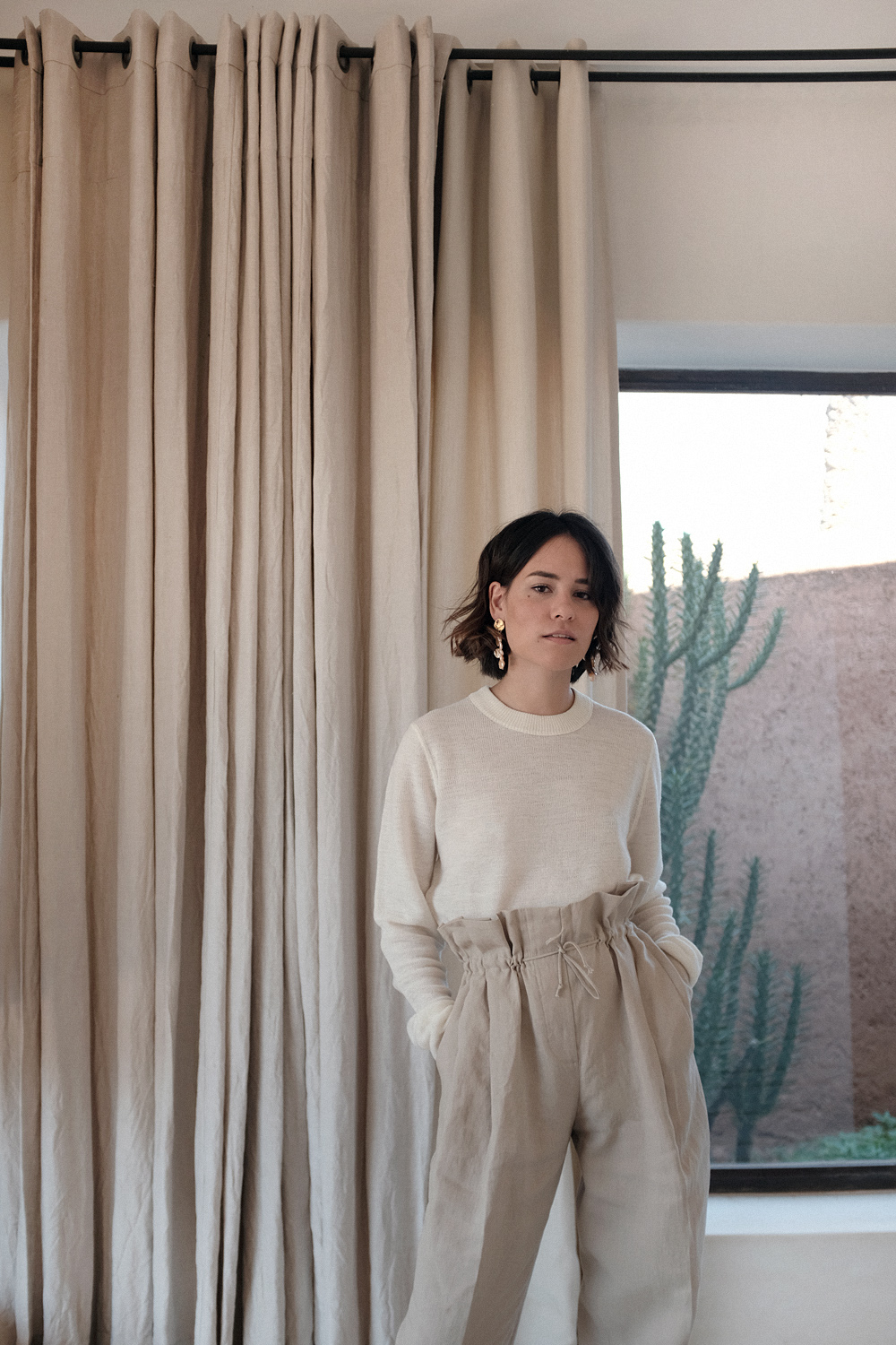 Nisi is wearing: Acne Studios Paperbag pants, Céline strap sandals, Wool crew neck shirt, The Row Ascot bag, Alighieri La Jetée earrings