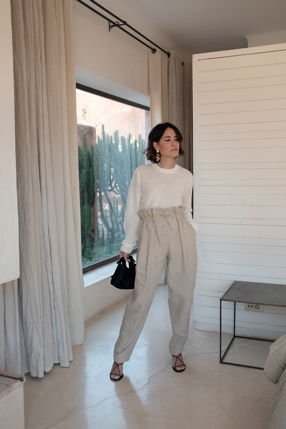 Nisi is wearing: Acne Studios Paperbag pants, Céline strap sandals, Wool crew neck shirt, The Row Ascot bag, Alighieri La Jetée earrings