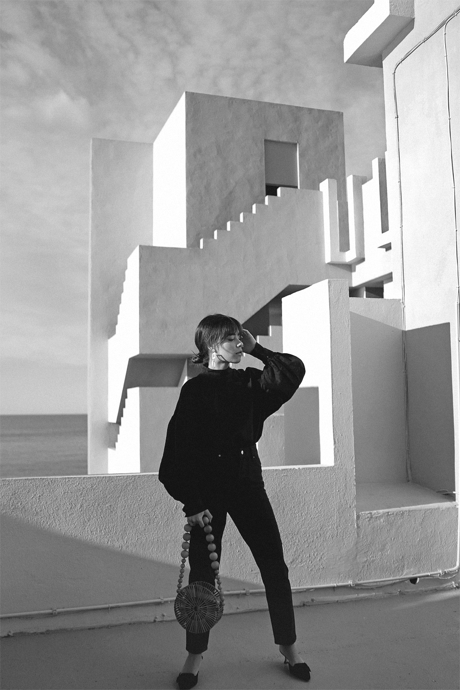 Outfit: Geometric Forms. Nisi is wearing: Cult Gaia Luna Bag, Manolo Blahnik Maysale Pumps, Mother-of-pearl earrings, Black mom jeans, Black high-neck blouse