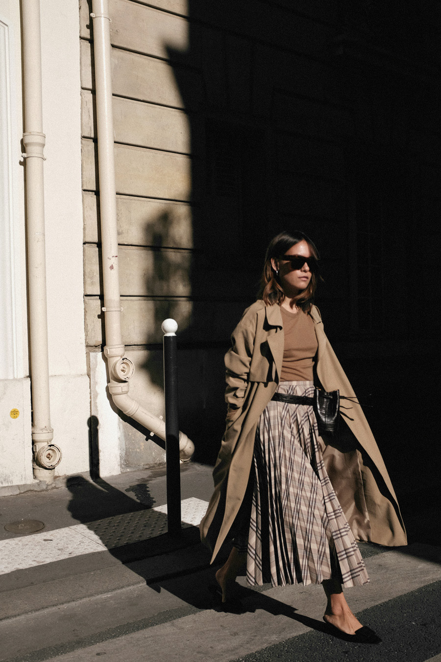 Nisi is wearing: Trenchcoat, Nanushka Belt bag, Manolo Blahnik Maysale mules, H&M Pleated skirt, Arket nude longsleeve top