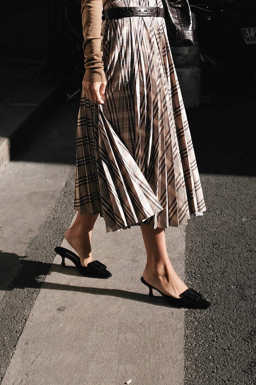 Nisi is wearing: Trenchcoat, Nanushka Belt bag, Manolo Blahnik Maysale mules, H&M Pleated skirt, Arket nude longsleeve top