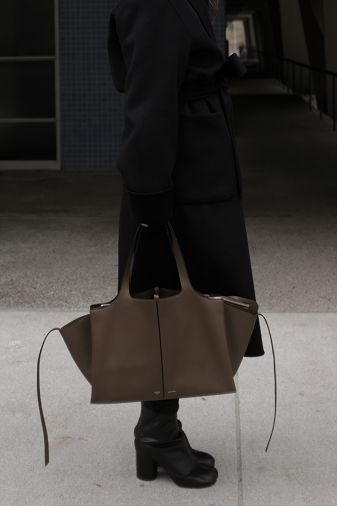 Desi is wearing: Maison Margiela Tabi boots, Céline Tri-Fold bag, Wrap coat, Knit jumper, Mom jeans L’Or Liquide maxi earrings by teetharejade