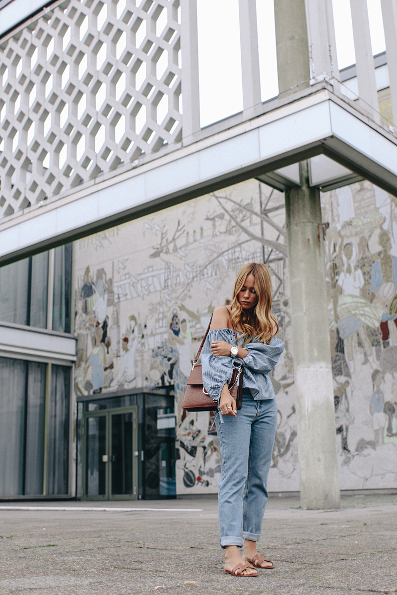 Desi is wearing: Gingham off-the-shoulder top, mom jeans, Hermès Oran sandals, Chloé Faye bag