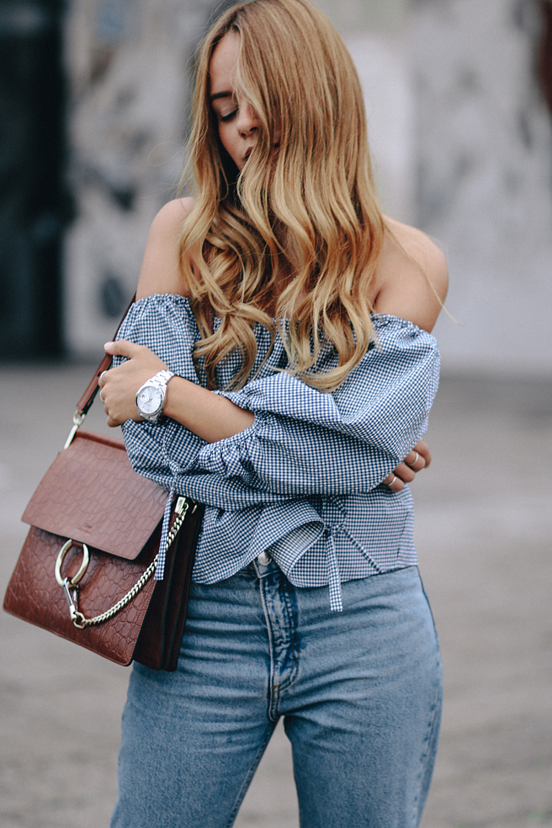 Desi is wearing: Gingham off-the-shoulder top, mom jeans, Hermès Oran sandals, Chloé Faye bag