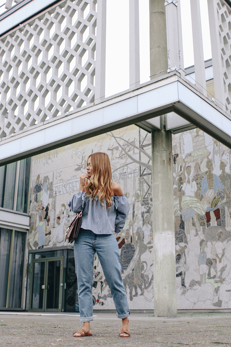 Desi is wearing: Gingham off-the-shoulder top, mom jeans, Hermès Oran sandals, Chloé Faye bag