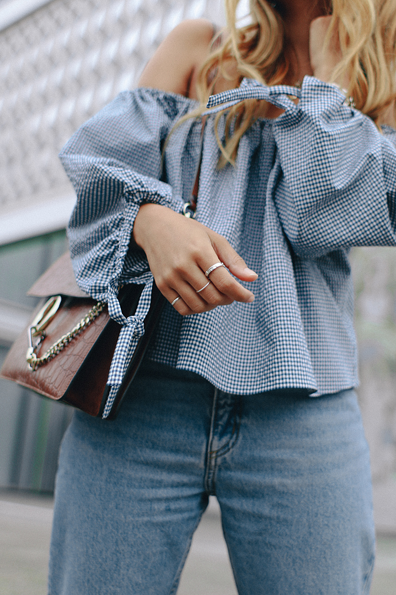 Desi is wearing: Gingham off-the-shoulder top, mom jeans, Hermès Oran sandals, Chloé Faye bag