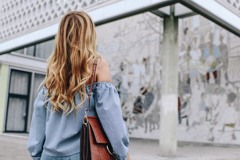 Desi is wearing: Gingham off-the-shoulder top, mom jeans, Hermès Oran sandals, Chloé Faye bag