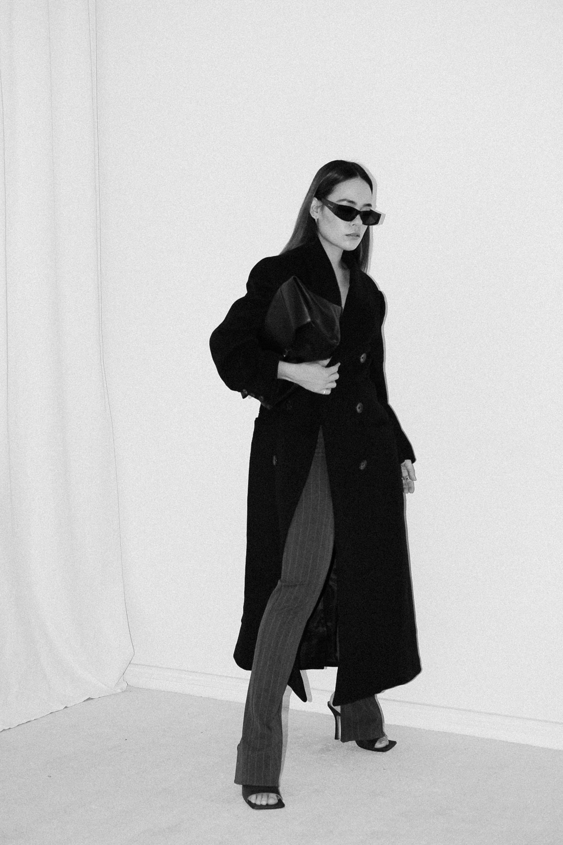 Desi wearing: Double breasted coat EDITED, Script-Logo sunglasses SAINT LAURENT, Silver hoops STILNEST, Pin-striped pants MANGO, Stretch mule sandals BOTTEGA VENETA, Big soft clutch CÉLINE, Silver watch KAPTEN & SON