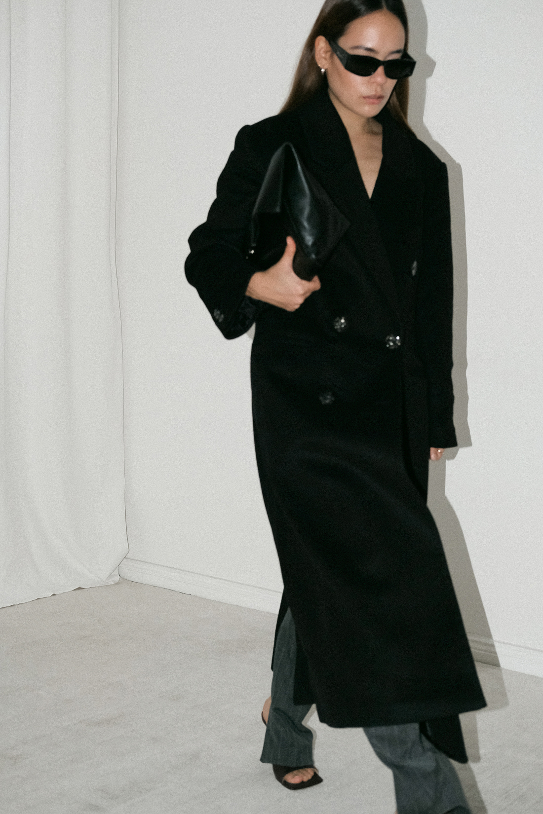 Desi wearing: Double breasted coat EDITED, Script-Logo sunglasses SAINT LAURENT, Silver hoops STILNEST, Pin-striped pants MANGO, Stretch mule sandals BOTTEGA VENETA, Big soft clutch CÉLINE, Silver watch KAPTEN & SON