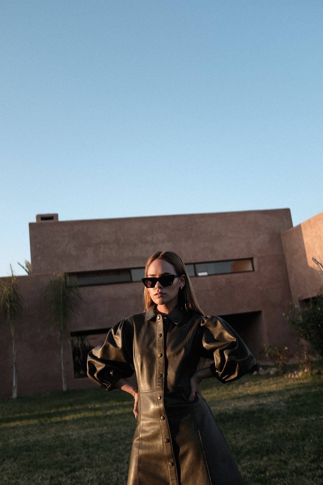Desi is wearing: Ganni Leather minidress, Rejina Pyo Zeo Strappy leather mules, Saint Laurent New Wave 276 cat-eye sunglasses, Earrings L’Or Liquide