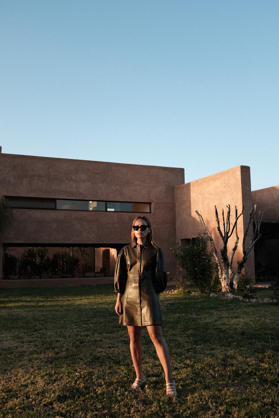 Desi is wearing: Ganni Leather minidress, Rejina Pyo Zeo Strappy leather mules, Saint Laurent New Wave 276 cat-eye sunglasses, Earrings L’Or Liquide