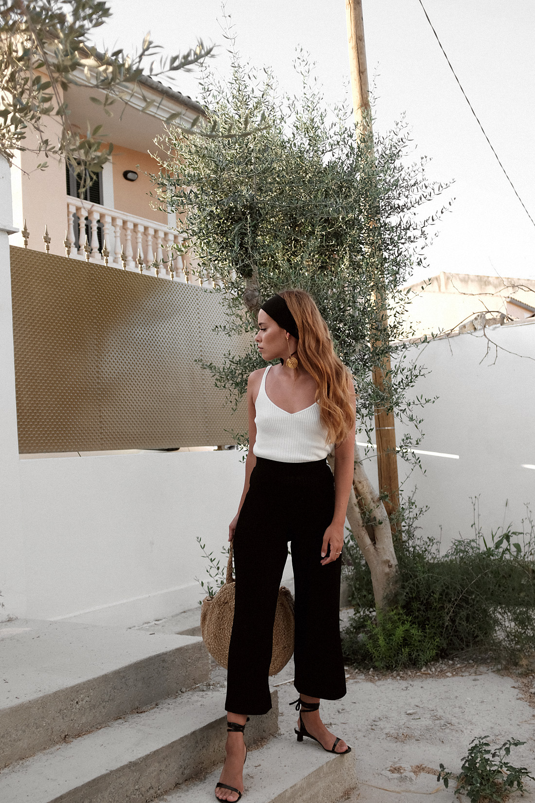 Jacquemus Le Carre earrinngs, Tibi strap sandals, round raffia bag, Tôteme headband, white ribbed top, black ribbed culottes