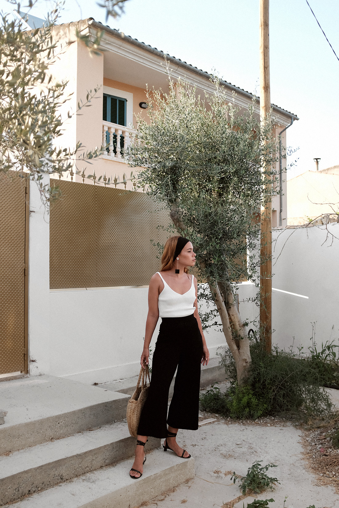 Jacquemus Le Carre earrinngs, Tibi strap sandals, round raffia bag, Tôteme headband, white ribbed top, black ribbed culottes