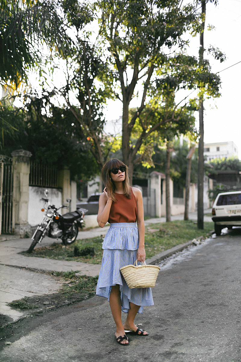Nisi is wearing: Straw bag, striped skirt with volants, Céline Baby Audrey sunglasses, Nina Kastens Stella Earrings, Hermès Oran sandals