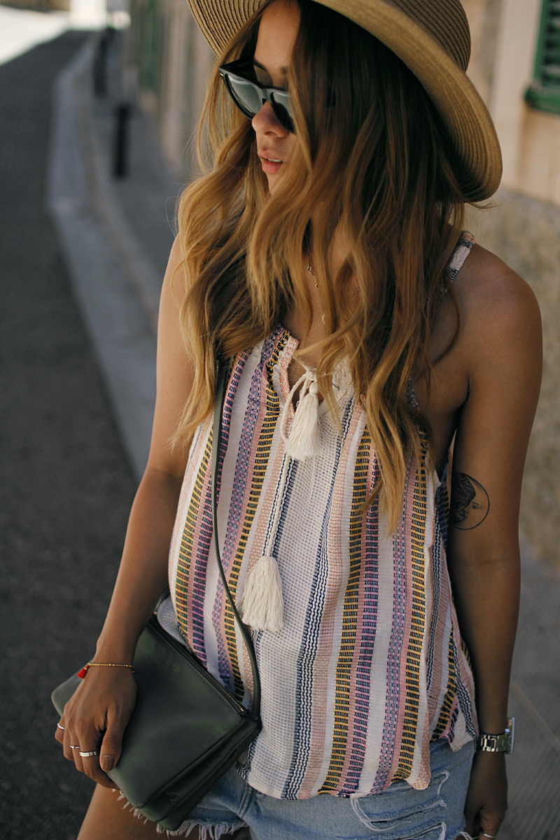 Desi is wearing: striped top with tassels, ripped cut-off denim shorts, Céline trio bag, straw hat - summer holiday look in Santanyí - Moon tattoo